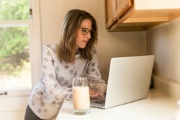 A woman using her laptop on her kitchen counter to create a budget using the 50 30 20 rule.