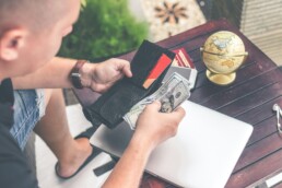 A man sitting at a table beside a closed laptop, going through his wallet and practicing financial literacy by budgeting his money.