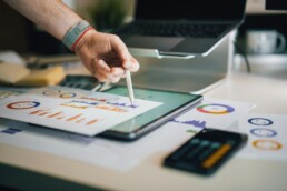 A person's hand using a stylus to point to financial charts they've set up to help in paying off debt