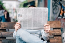 A man reading a newspaper on a bench, trying to stay informed about finance news.