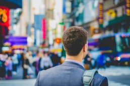 A view from behind of a young investor in a suit walking in a crowded city