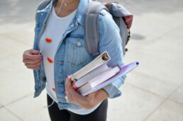 A young student who used student loans, carrying a stack of binders