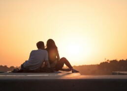 A couple sitting on a wooden deck, having financial conversations as they watch the sunset