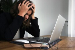 A person experiencing financial stress, sitting in front of a laptop and cradling their head